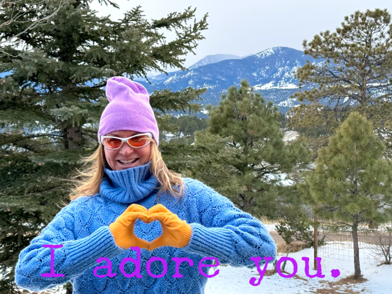 Sonja Stilp, MD pictured outside in the Colorado mountains in winter forming the shape of a heart with her hands. The words "I Adore You" are typed at the bottom over the photo.