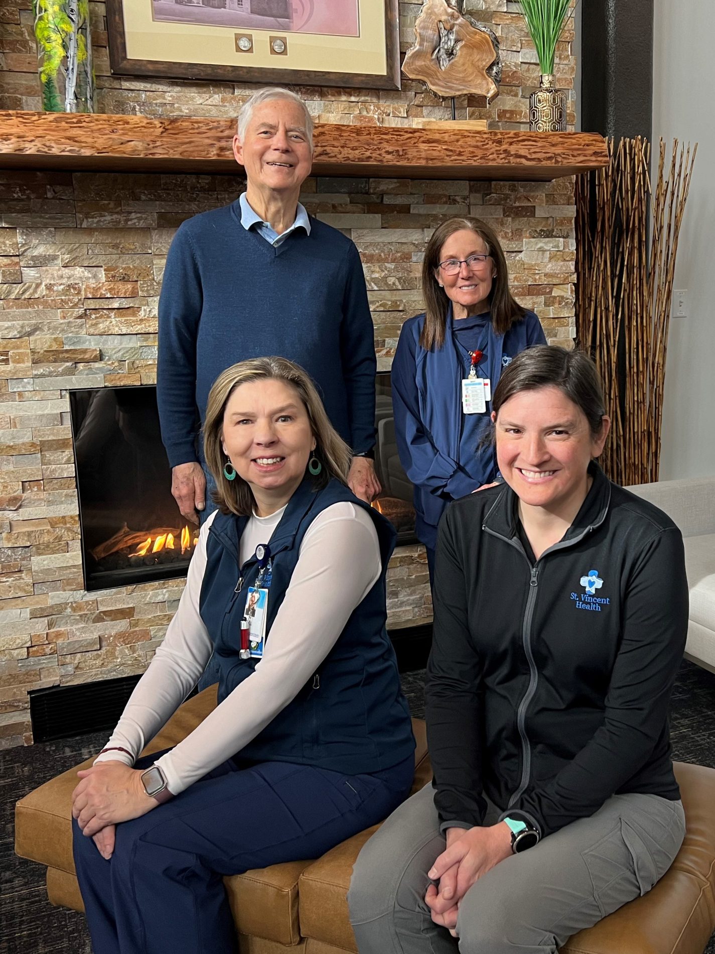 Patient, Brad Smith is in front of a fireplace with Deb Cunningham, RN, Eileen Johnson, RN, and Kelly Bergkessel, PT. Team members at St. Vincent health who provided compassionate close to home.