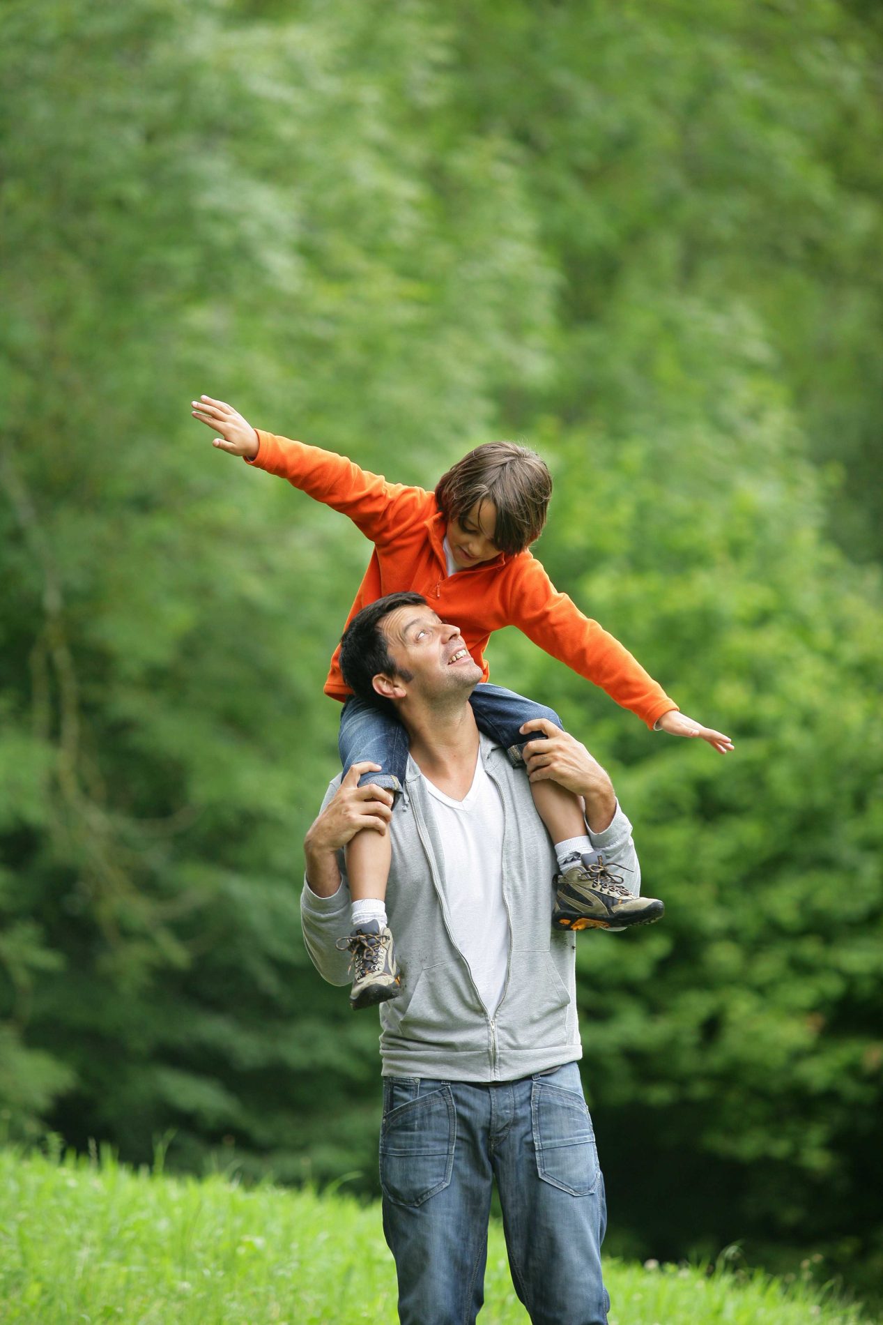man with son on his shoulders outdoors walking through a grassy area.